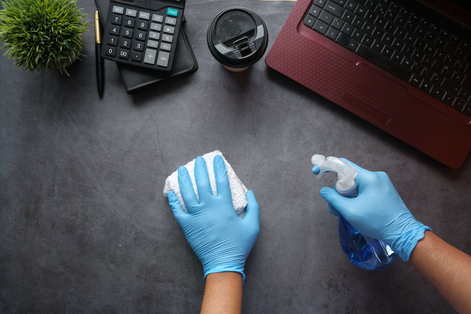 Gloved hands disinfecting a desk with a cloth and spray bottle